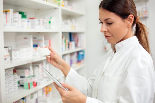 Medicine, pharmaceutics, health care and people concept - Serious young female pharmacist taking medications from the shelf.